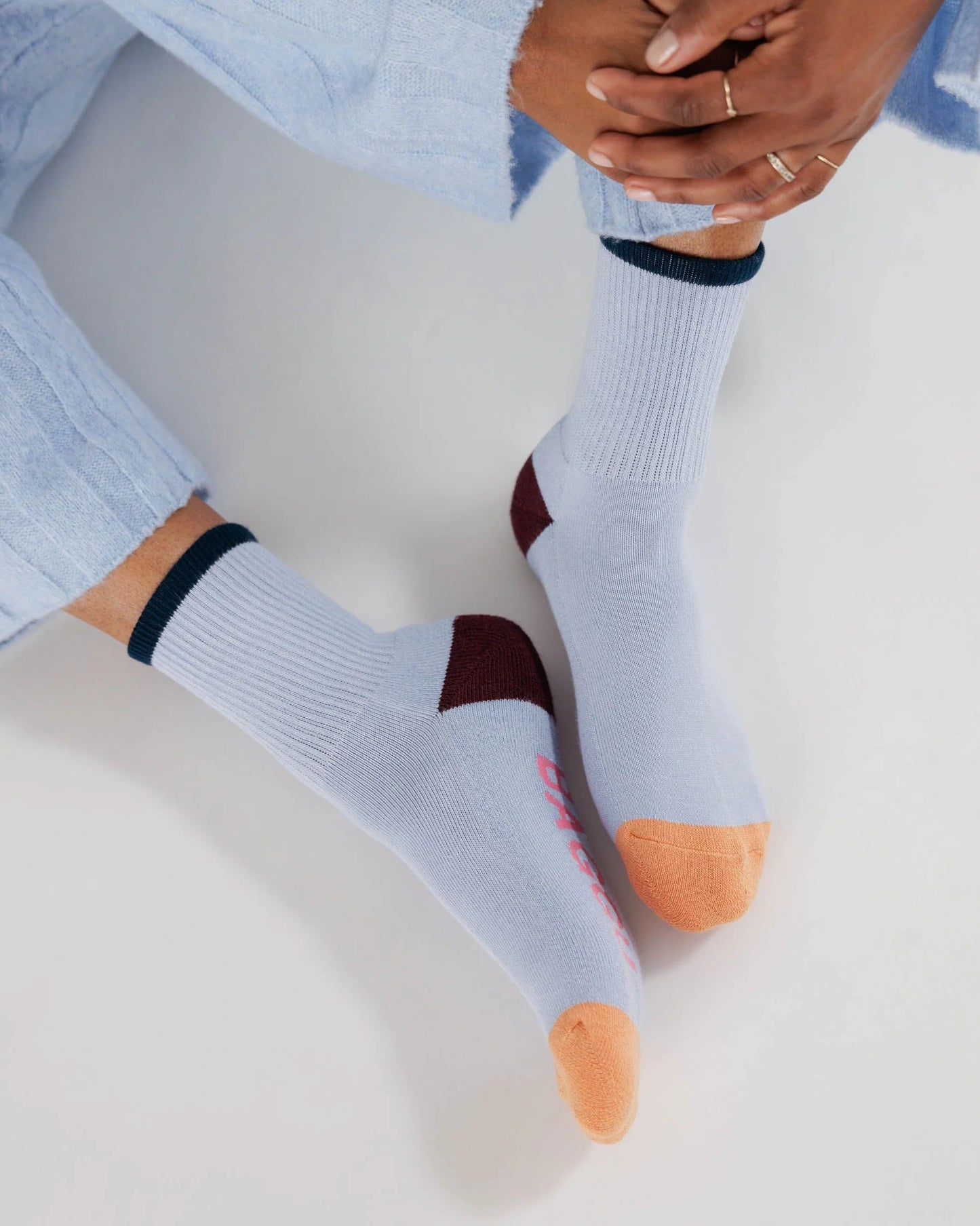 Light Blue Socks with black Ankle Stripe, Brown heel, orange colour blocked toes, and pink "BAGGU" text on bottom of feet